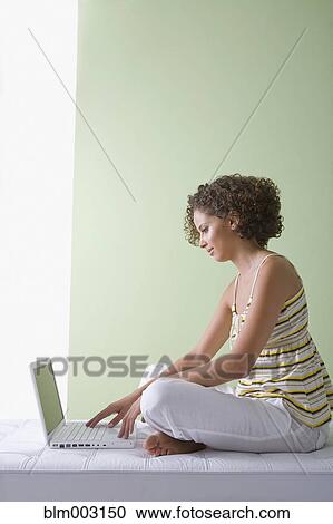 Stock Image - Mixed race woman sitting on sofa using laptop. Fotosearch