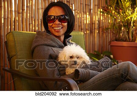 Stock Image - Mixed race woman sitting with dog outdoors. Fotosearch