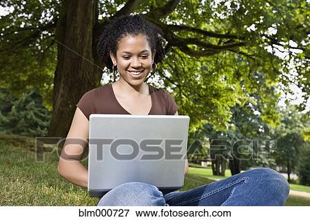 Stock Photo - Mixed race woman typing on laptop outdoors. Fotosearch
