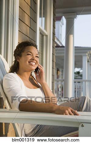 Stock Photo - Mixed race woman using cell phone on porch. Fotosearch
