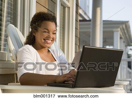 Stock Photo - Mixed race woman using laptop on porch. Fotosearch