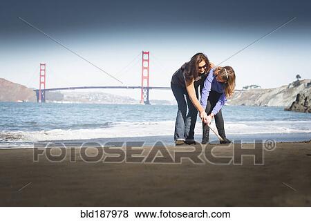 Stock Photo - Mother and daughter drawing in sand on beach, San Francisco, California, United States. Fotosearch