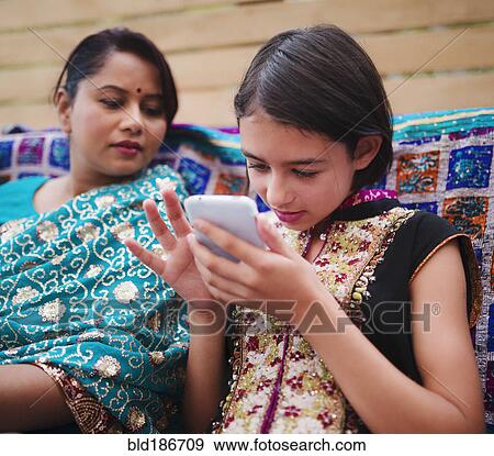 Mother and daughter in Indian clothing using cell phone View Large Photo Image Stock Photo - Mother and daughter in Indian clothing using cell phone. Fotosearch