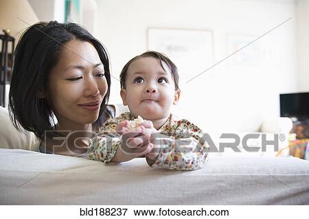 Stock Photo - Mother and daughter sitting on sofa. Fotosearch