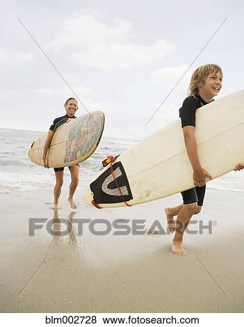 Stock Photo - Mother and son carrying surfboards out of water at beach. Fotosearch