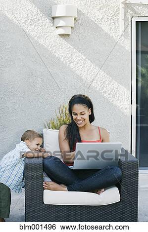 Stock Photograph - Mother and son looking at laptop on patio. Fotosearch