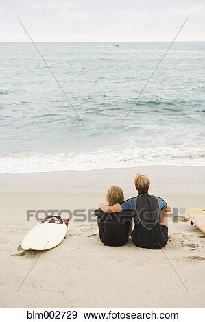 Mother and son sitting on beach next to surfboard View Large Photo Image Stock Photo - Mother and son sitting on beach next to surfboard. Fotosearch