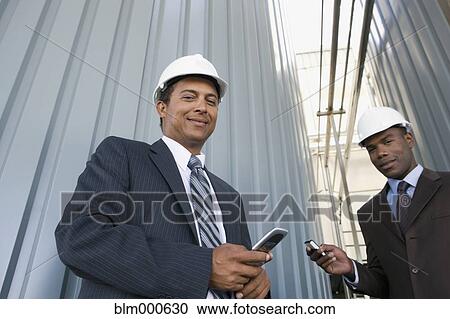 Stock Image - Multi-ethnic businessmen in hard-hats holding cell phones. Fotosearch
