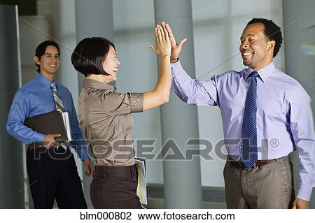 Stock Image - Multi-ethnic co-workers high fiving in office. Fotosearch