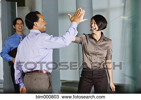 Stock Image - Multi-ethnic co-workers high fiving in office. Fotosearch