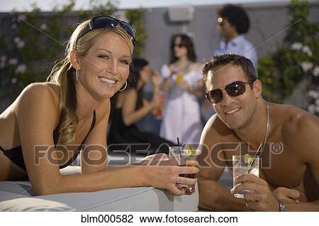 Stock Image - Multi-ethnic couple drinking cocktails poolside. Fotosearch