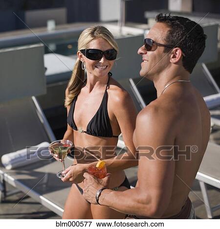 Stock Photo - Multi-ethnic couple drinking cocktails poolside. Fotosearch