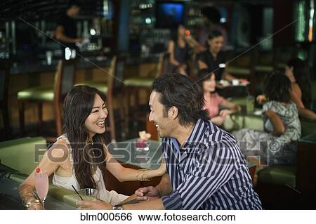Stock Photograph - Multi-ethnic couple drinking cocktails in nightclub. Fotosearch