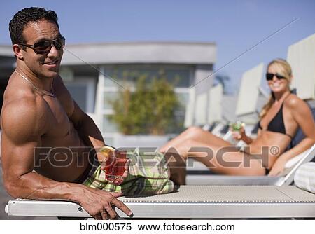 Stock Photography - Multi-ethnic couple drinking cocktails poolside. Fotosearch