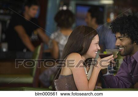 Stock Image - Multi-ethnic couple drinking martinis in nightclub. Fotosearch