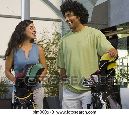 Stock Image - Multi-ethnic couple holding golf bags. Fotosearch