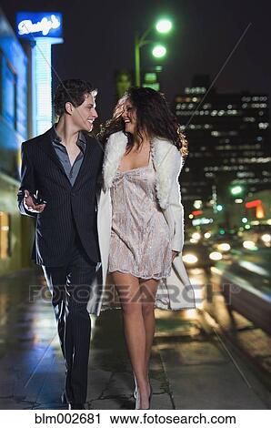 Stock Image - Multi-ethnic couple in formal attire walking down sidewalk. Fotosearch