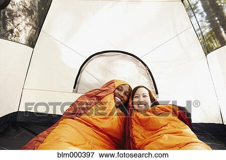 Stock Photo - Multi-ethnic couple inside sleeping bags and tent. Fotosearch