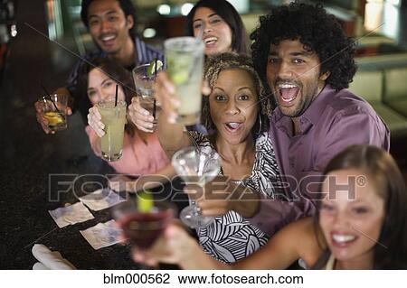 Stock Image - Multi-ethnic friends drinking cocktails in nightclub. Fotosearch