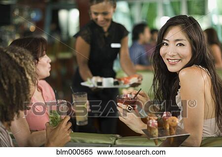 Stock Photography - Multi-ethnic friends drinking cocktails and having sushi in nightclub. Fotosearch