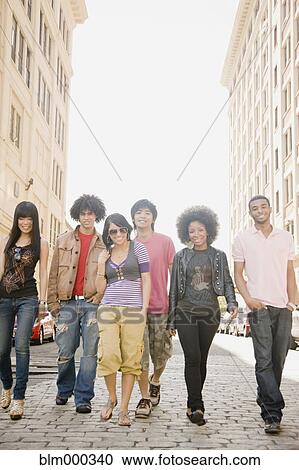 Stock Image - Multi-ethnic friends walking down urban sidewalk. Fotosearch