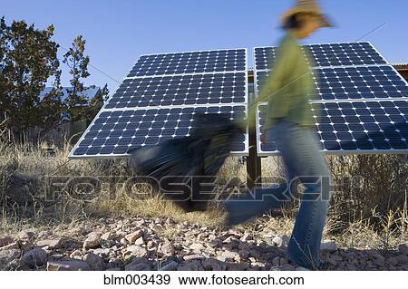 Stock Photo - Native American woman carrying bag past solar panels. Fotosearch