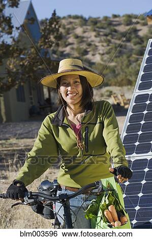 Stock Photograph - Native American woman on bicycle near solar panels. Fotosearch