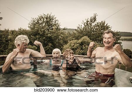 Stock Image - Older Caucasian couples relaxing in swimming pool. Fotosearch
