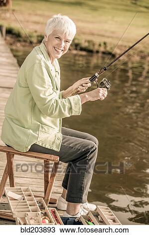 Stock Image - Older Caucasian woman fishing in rural lake. Fotosearch