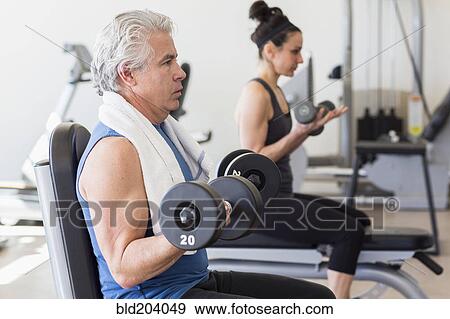 Stock Photo - Older Hispanic man lifting weights in gym. Fotosearch