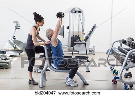 Stock Photo - Older Hispanic man working with trainer in gym. Fotosearch