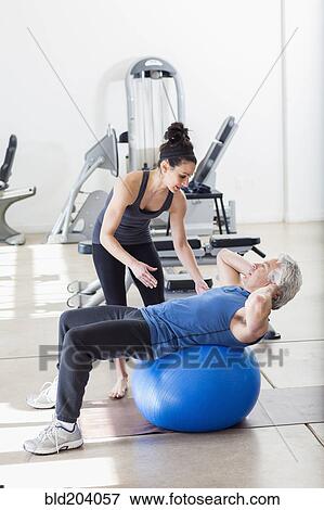 Stock Photo - Older Hispanic man working with trainer in gym. Fotosearch