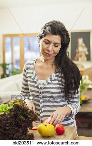 Stock Image - Older Hispanic woman chopping fruit in kitchen. Fotosearch