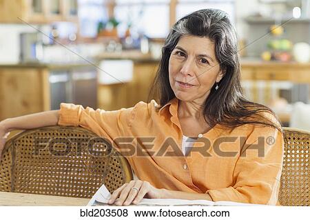 Stock Photo - Older Hispanic woman reading newspaper at table. Fotosearch