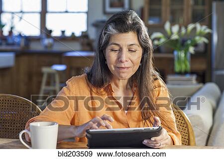Stock Photo - Older Hispanic woman using tablet computer at table. Fotosearch