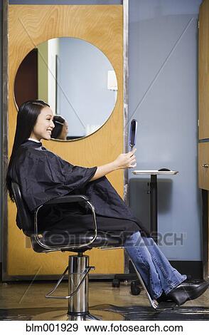 Stock Photo - Pacific Islander woman looking at hair in salon. Fotosearch