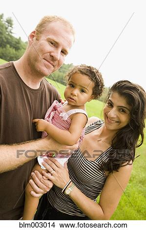 Picture - Parents holding mixed race daughter outdoors. Fotosearch