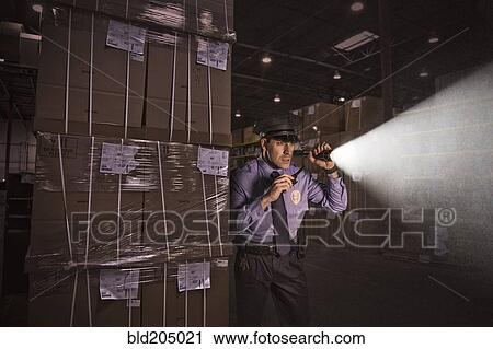 Stock Image - Police officer shining flashlight in warehouse. Fotosearch