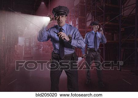 Stock Image - Police officers using walkie talkies in warehouse. Fotosearch