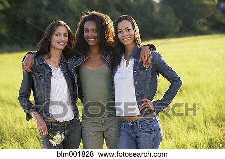 Stock Photo - Portrait of three women hugging in meadow. Fotosearch