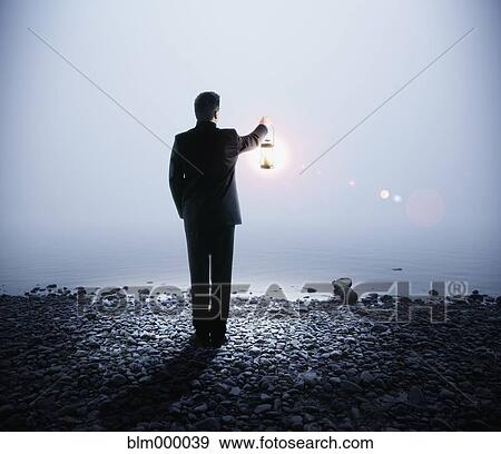 Stock Photo - Portuguese businessman holding lantern next to water. Fotosearch
