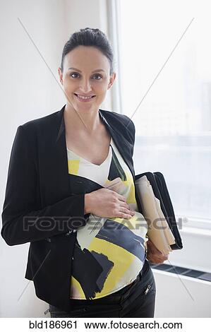 Stock Image - Pregnant Caucasian businesswoman standing in office. Fotosearch