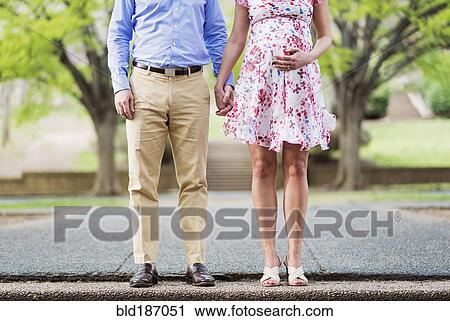 Stock Image - Pregnant Caucasian couple holding hands outdoors. Fotosearch