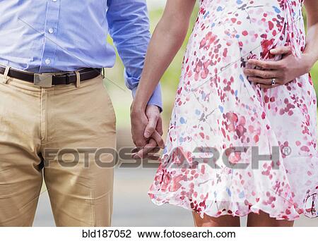 Stock Image - Pregnant Caucasian couple holding hands outdoors. Fotosearch