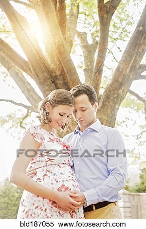 Stock Photography - Pregnant Caucasian couple hugging outdoors. Fotosearch
