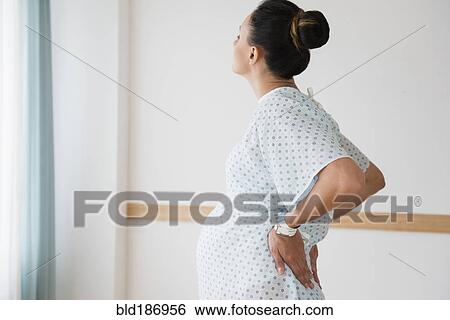 Stock Photograph - Pregnant Caucasian with back pain in hospital gown. Fotosearch