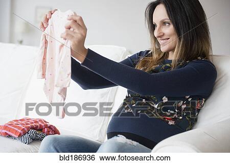 Stock Photograph - Pregnant Caucasian woman admiring baby clothing. Fotosearch