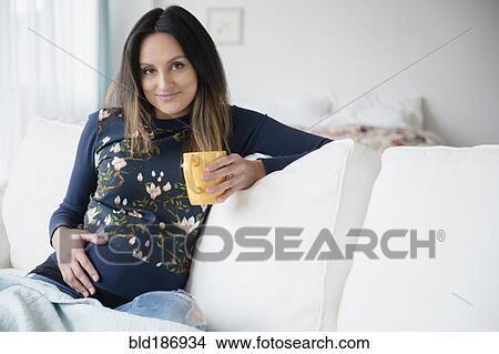 Pregnant Caucasian woman drinking cup of coffee on sofa View Large Photo Image Picture - Pregnant Caucasian woman drinking cup of coffee on sofa. Fotosearch