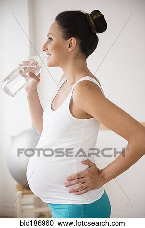 Stock Image - Pregnant Caucasian woman drinking water bottle. Fotosearch