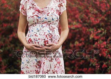 Stock Image - Pregnant Caucasian woman holding her belly outdoors. Fotosearch